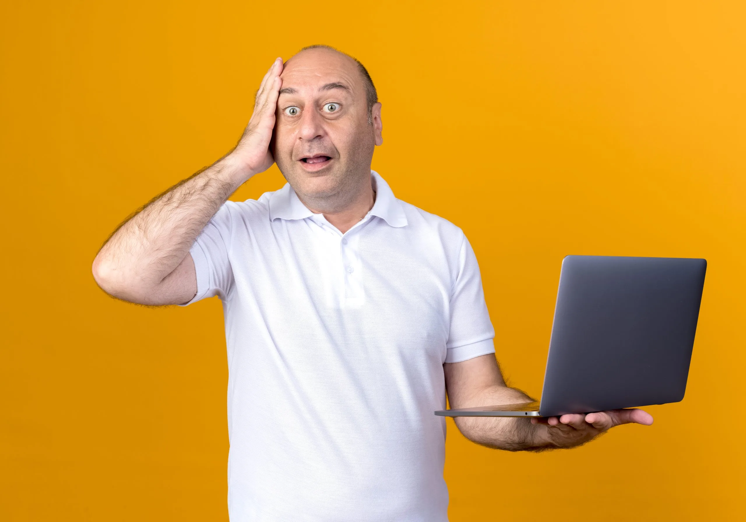 surprised casual mature man holding laptop and putting hand on forehead isolated on yellow backgound